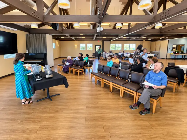 Presenter speaking beside a projection screen during a seminar in the fellowship hall