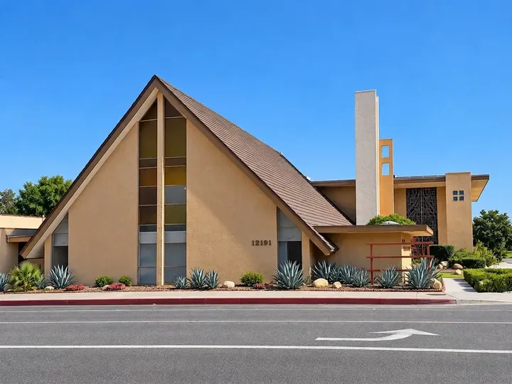 Front of the sanctuary building with a steep brown roof, tall windows and agave landscaping