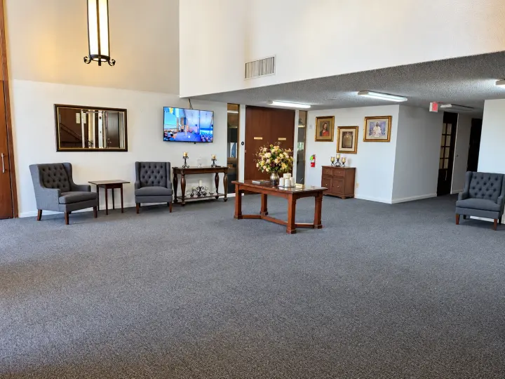 Carpeted main lobby with armchairs, a coffee table with flowers and a wall-mounted screen