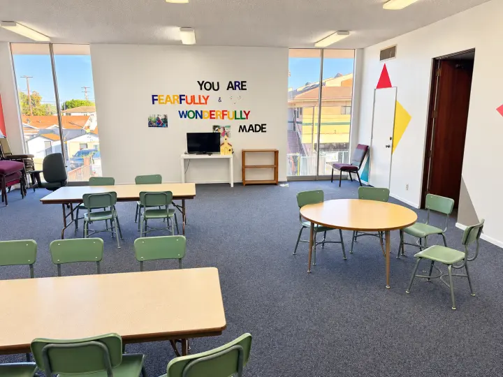 Children's classroom with small tables, green chairs and a 'You are fearfully and wonderfully made' wall
