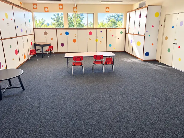 Children's classroom with white cabinets decorated with colorful dots and a small table with red chairs