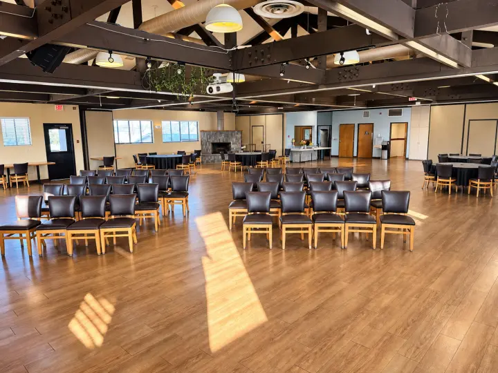 Fellowship hall set with rows of padded chairs facing forward, with round tables at the sides