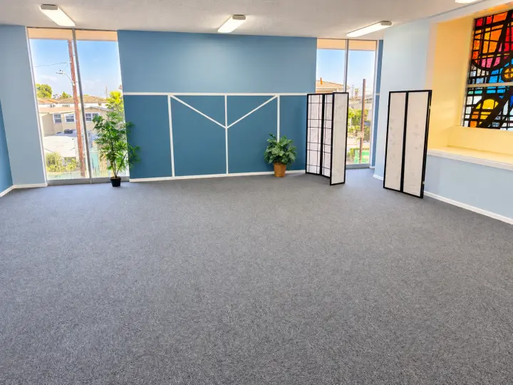 Carpeted multipurpose room with a blue accent wall, folding screens, plants and stained glass