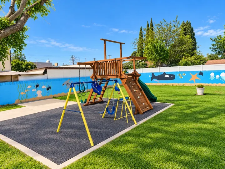 Fenced church playground with a swing set, climbing wall and slide on soft safety surfacing, with an ocean mural on the wall